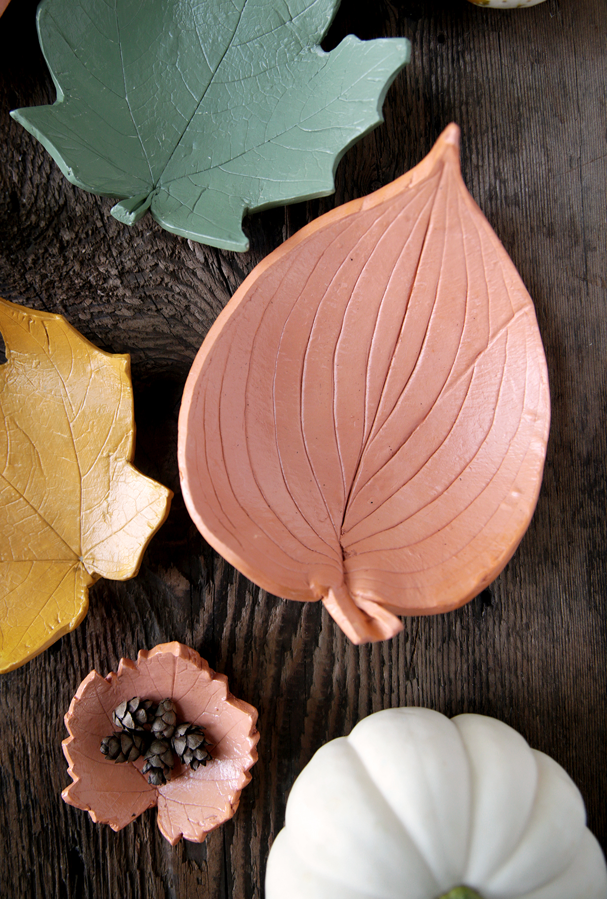 terracotta large clay leaf bowl sitting on wood with other clay leaves and pumpkin